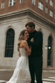 a man and woman standing in front of a building hugging each other on the street