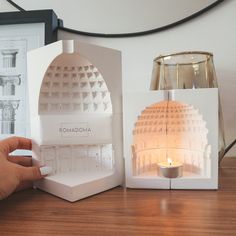 a person holding a lit candle in front of a paper cut out of a building