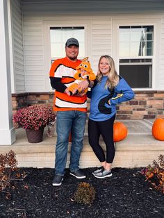 a man and woman standing in front of a house with pumpkins on the porch