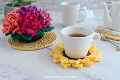 there is a cup and saucer on the table with crocheted coasters