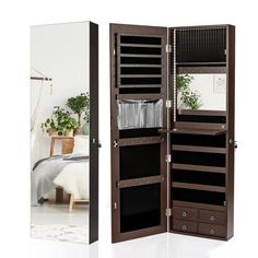 an open wooden jewelry cabinet next to a mirror and potted plant on the floor