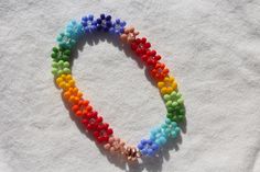 a multicolored beaded necklace on a white cloth with an orange, yellow, green, and blue flower charm