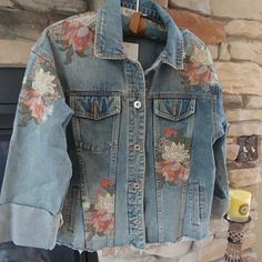 a denim jacket with flowers on it hanging from a fireplace mantel in front of a brick wall