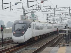 a white train traveling down tracks next to a tall building with lots of power lines above it