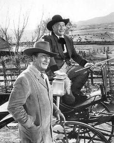 black and white photograph of two men in cowboy hats standing next to a horse drawn carriage