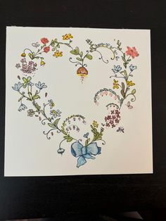 a card with flowers and butterflies in the shape of a heart on top of a table