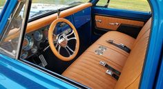 the interior of an old blue car with tan leather seats and steering wheel, in front of a grassy area