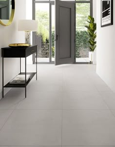 a hallway with white walls and flooring has an open door leading to another room