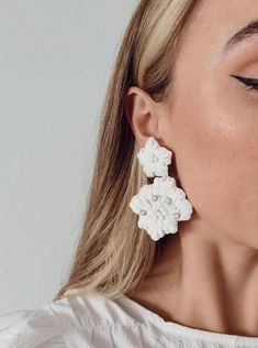 a woman wearing large white flower earrings