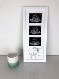 a framed photograph with two baby shoes on it next to a cup