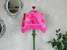 a pink lamp on a green table next to a mirror and potted plant in front of it