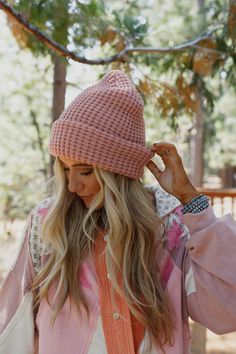 a woman with long hair wearing a pink knitted hat and scarf, standing in the woods