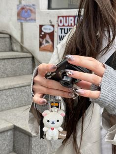 a woman with long nails holding a camera in her hand and a small bear keychain