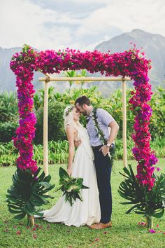 a man and woman standing under a pink flower arch