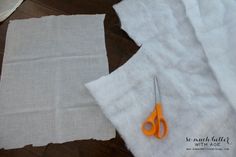 two pieces of white fabric with orange scissors on them next to some cut linens