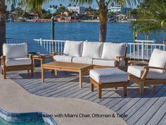 a couch and table on a deck next to the water with palm trees in the background