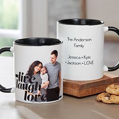 two black and white coffee mugs sitting next to each other on a wooden cutting board