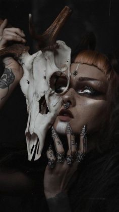 a woman with her face painted white and holding a deer's skull in front of her face