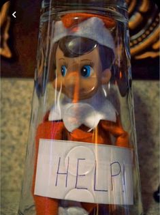 a glass jar with an elf in it that says help on the bottom and inside