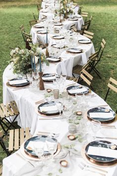 a long table is set with plates and place settings for an outdoor dinner party in the grass