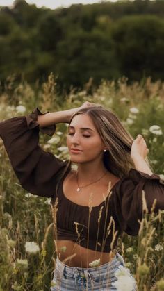 a beautiful young woman standing in a field of tall grass with her hands on her head