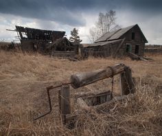 an old wooden house in the middle of a dry grass field with broken down windows