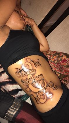 a woman's stomach with music notes and hearts tattoo on her side ribcage