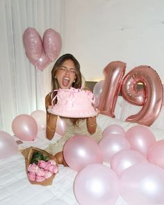 a woman holding a pink cake in front of balloons and the word mom spelled out