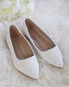 two white shoes sitting on top of a fur covered floor next to a bouquet of flowers