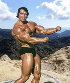 a man posing on top of a mountain with his arms and legs spread out, flexing