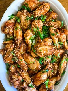 a white bowl filled with chicken wings covered in sesame seeds and garnishes