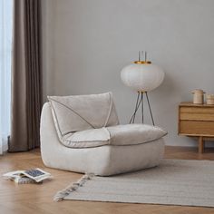 a white chair sitting on top of a hard wood floor next to a tall lamp