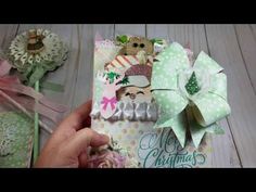 a hand holding an open christmas card with paper flowers and ribbon around it on a wooden table