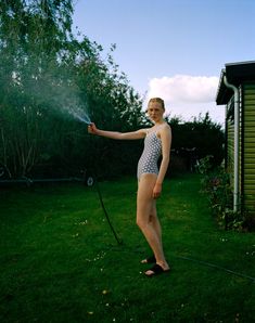 a woman in a bathing suit sprays water on her body with a garden hose