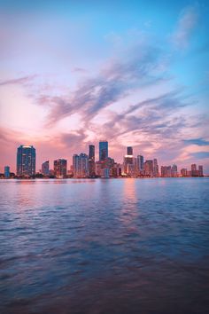 the city skyline is lit up at night with lights reflecting in the water and clouds