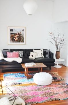 a living room with black couches and colorful rugs on the wooden flooring