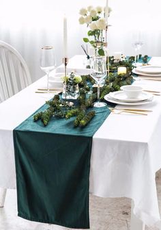 the table is set with white plates and green napkins on it, along with greenery