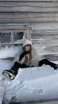 a person sitting in the snow with a snowboard on their feet and wearing a face mask