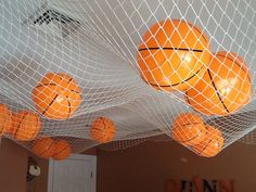 several oranges are suspended in a net with basketballs hanging from the ceiling above them