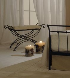 two lit candles sit on the floor in front of a wrought iron bed with white curtains