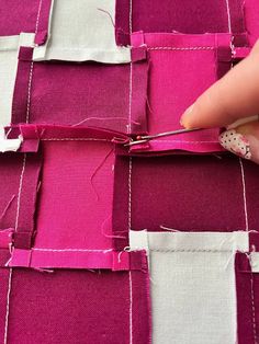 someone using scissors to cut fabric with pink and white squares in the background that are stitched together