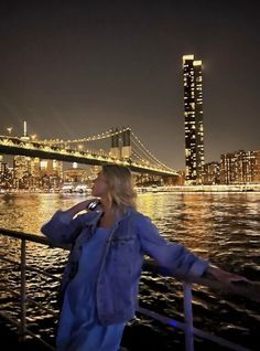 a woman standing on the side of a boat talking on a cell phone at night