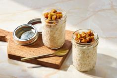 two jars filled with food sitting on top of a wooden tray next to a spoon