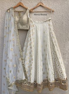 This white and gold threadwork blouse is paired with a multi kali butti lehenga with borders at the hem.  The outfit is completed with a tulle dupatta with a mirror work border and scattered buttis. Luxury White Choli With Cutdana, Luxury White Georgette Lehenga, Luxury White Choli With Dori Work, Luxury White Blouse For Navratri, Luxury Chanderi Choli For Diwali, Luxury White Chinon Choli, Luxury Off-white Sharara For Navratri, Luxury Semi-stitched Bohemian Choli, Luxury Off White Traditional Wear With Mirror Work