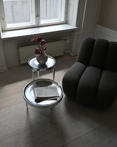 a chair and table in front of a window with a vase on the floor next to it