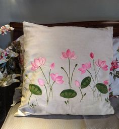 a white pillow with pink flowers on it sitting on a bed next to a potted plant