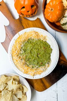 a white plate topped with guacamole and chips next to two pumpkins