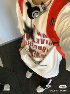 a boy with headphones on taking a selfie in the mirror while wearing a white shirt and red backpack