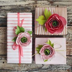 three wrapped gift boxes with paper flowers on them, one is pink and the other is green