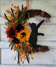 a black cat sitting on top of a wreath with sunflowers and other flowers